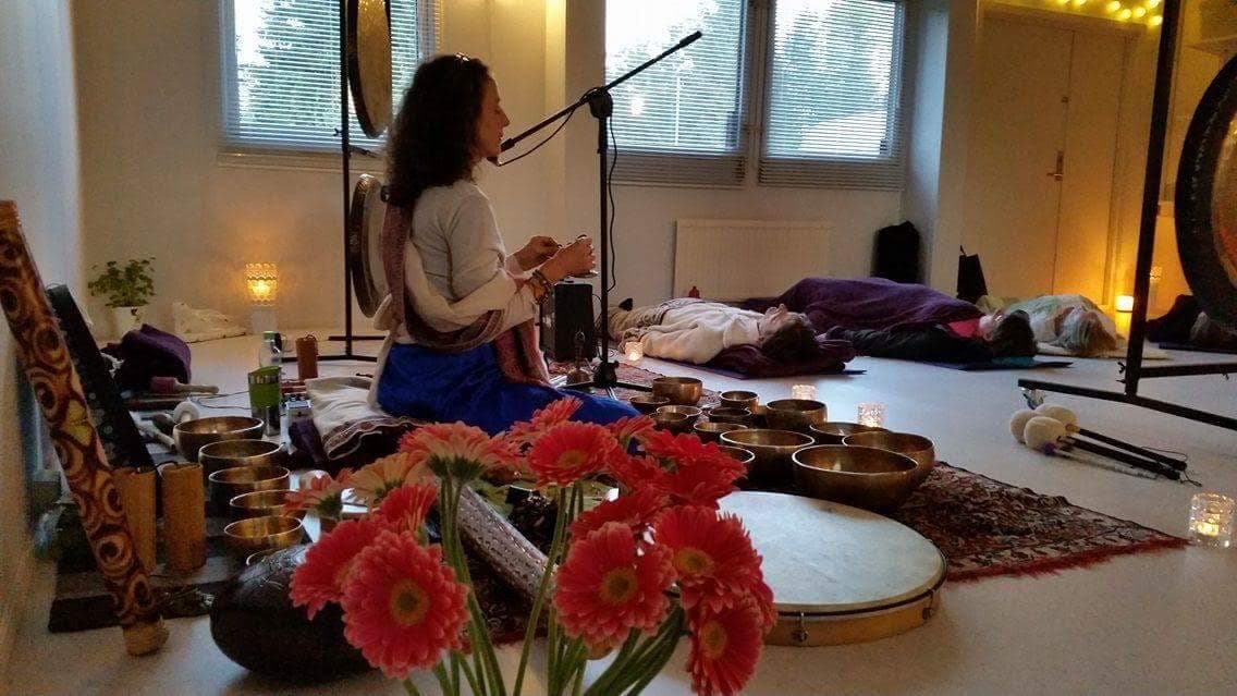 Tal playing singing bowls while participants lie on mattresses during a Sound Shower